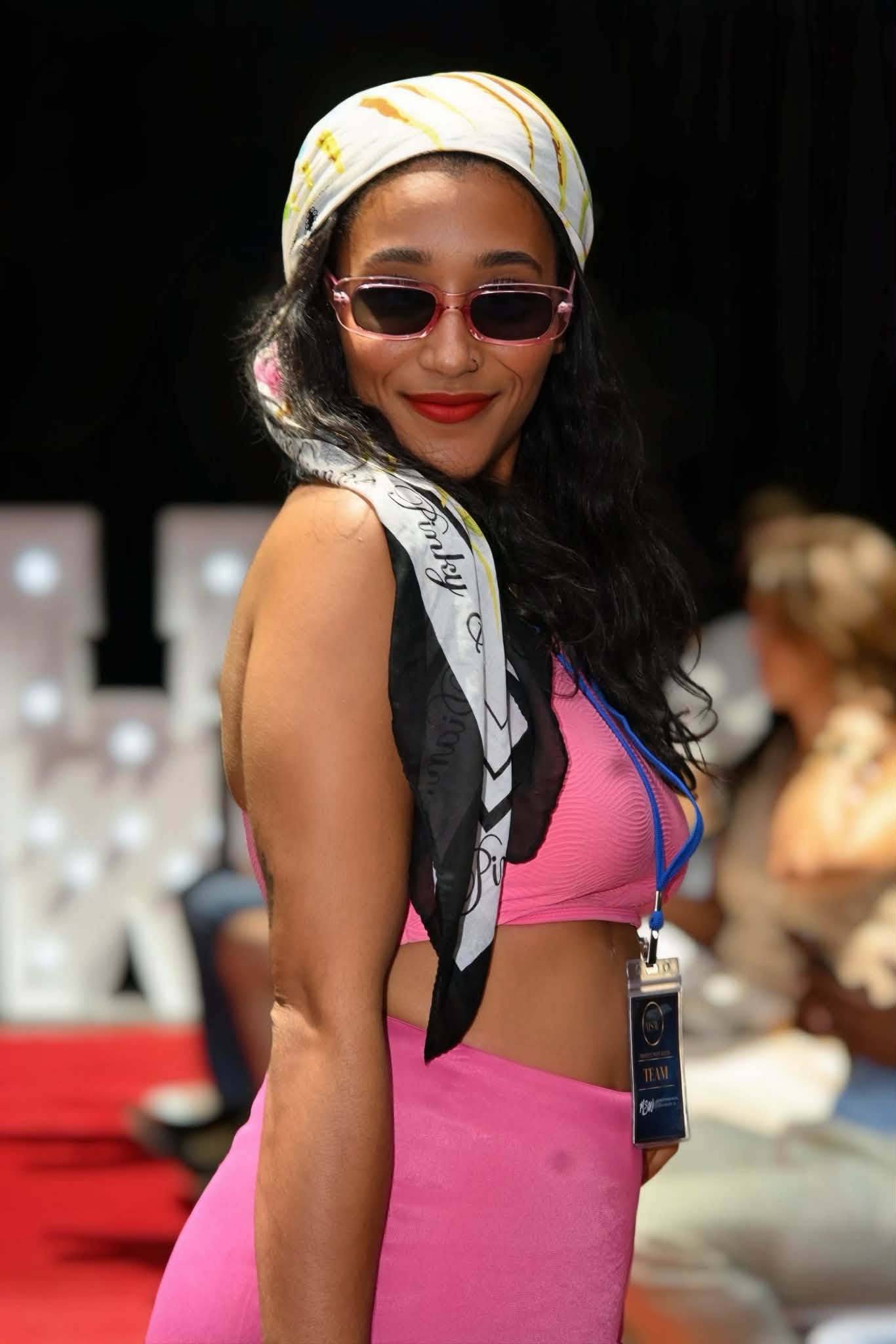 Runway portrait of a model wearing sunglasses, a headscarf, and pink swimwear